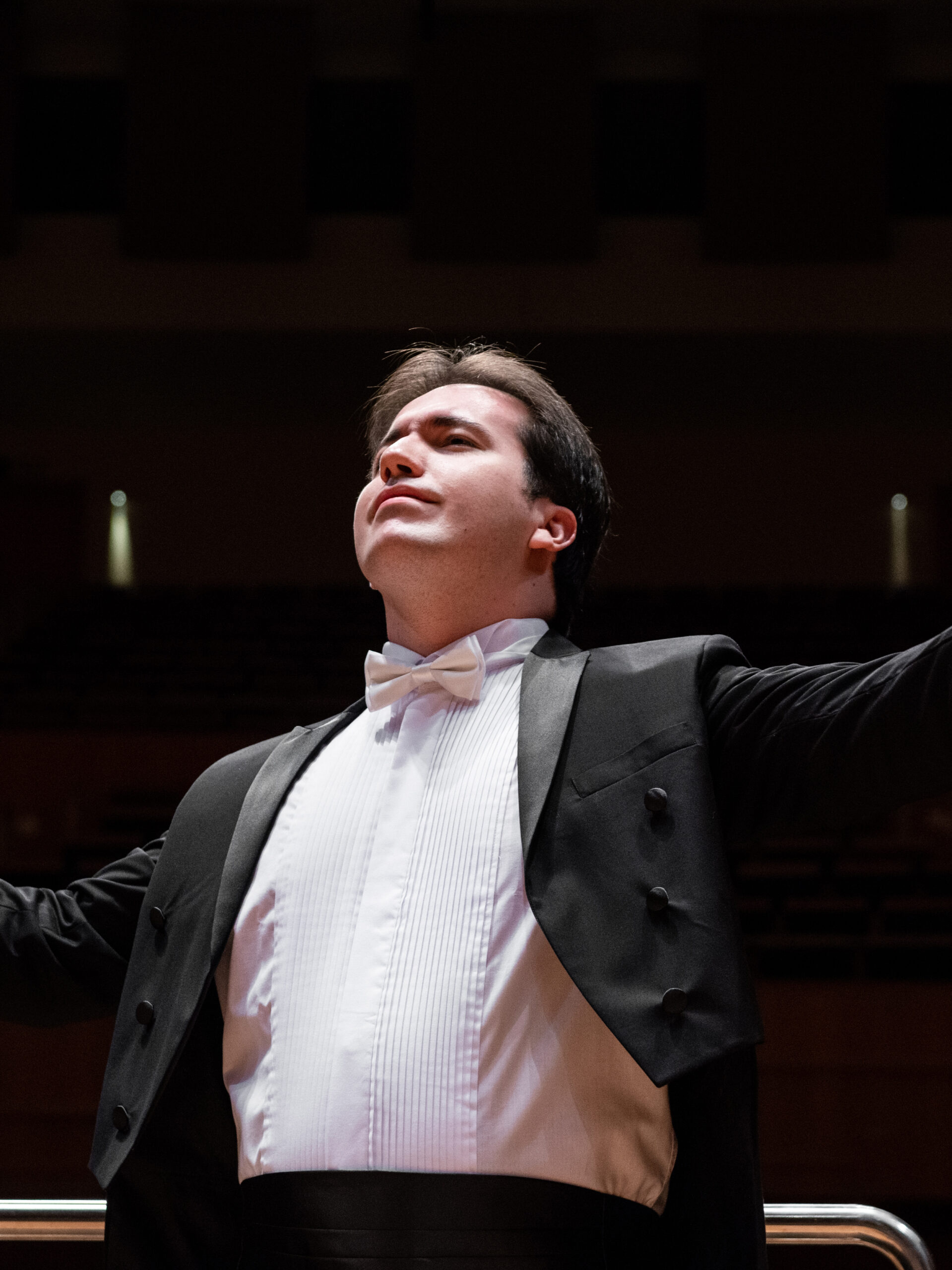 foto do maestro José Soares. Ele está regente um concerto e olhando para cima com os braços abertos.