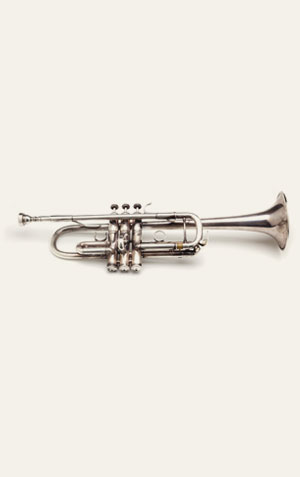 Foto de um trompete, um instrumento de sopro de metal com uma forma alongada e uma campana em forma de sino na extremidade. O trompete possui três válvulas que o músico usa para mudar a altura das notas.