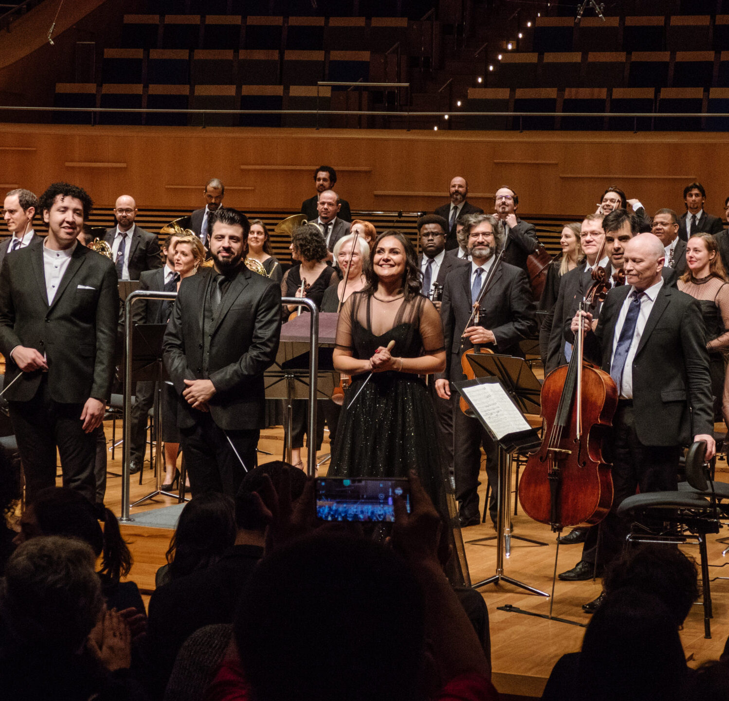 Foto mostrando os quatro regentes ativos do laboratório de regência em cima do palco. Eles estão recebendo os aplausos do público ao final do concerto. Foto de Felipe GIubilei.