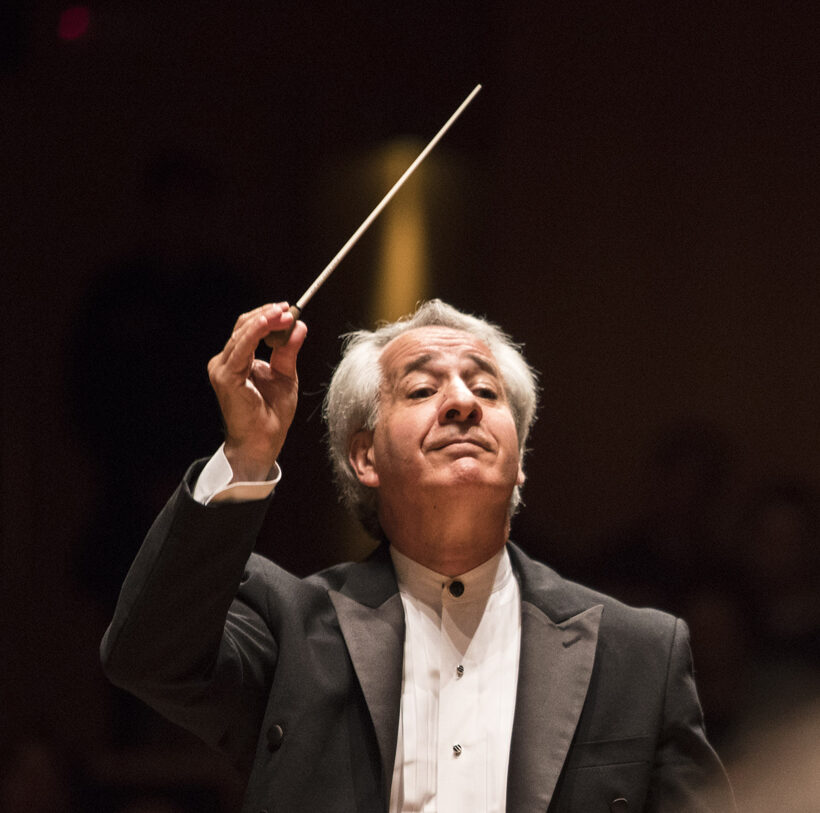 Foto do maestro Fabio Mechetti. Ele está regendo a orquestra. Somente sua mão esquerda, segurando a batuta, está levantada. Foto de Rafael Motta.