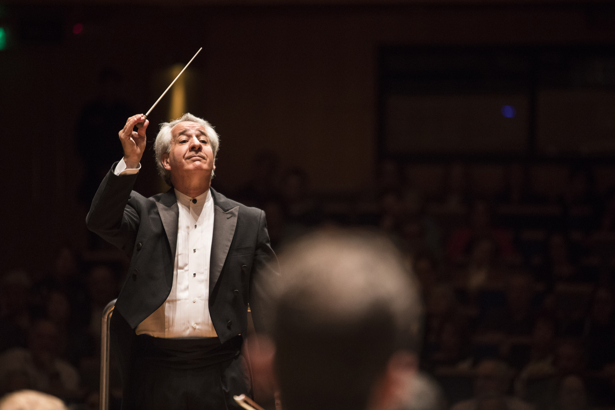 Foto do maestro Fabio Mechetti. Ele está regendo a orquestra. Somente sua mão esquerda, segurando a batuta, está levantada. Foto de Rafael Motta.
